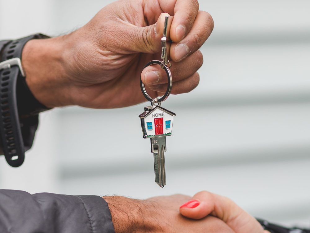 House key on a keychain being handed to a new resident over a handshake