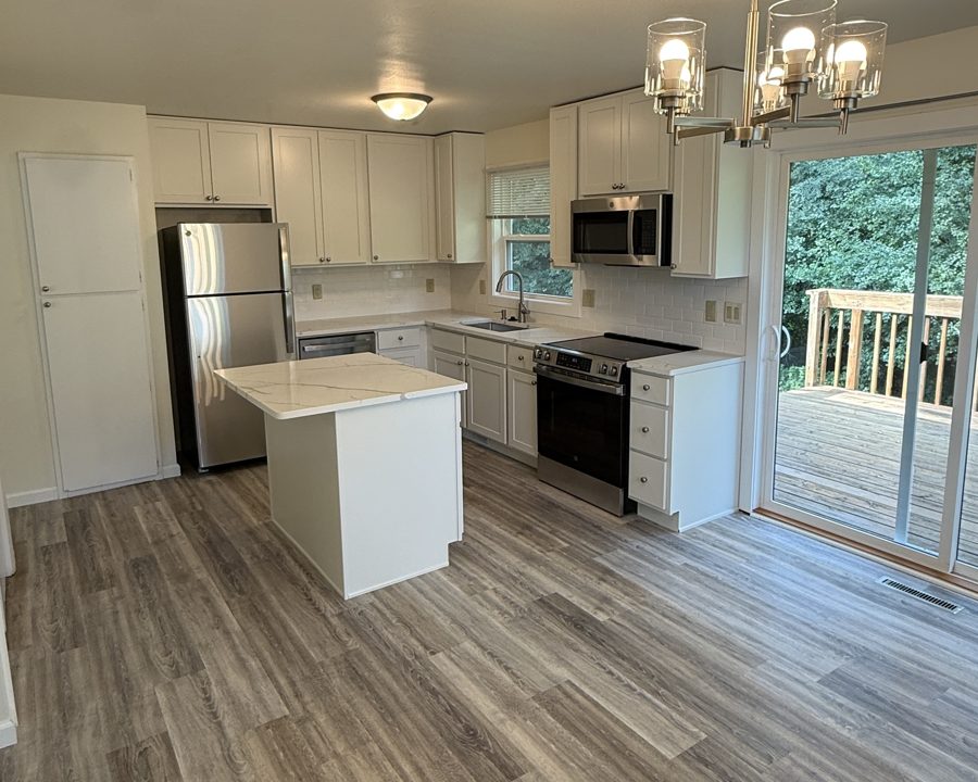 Updated kitchen with white shaker cabinets, stainless steel appliances, an island and a sliding door to a deck