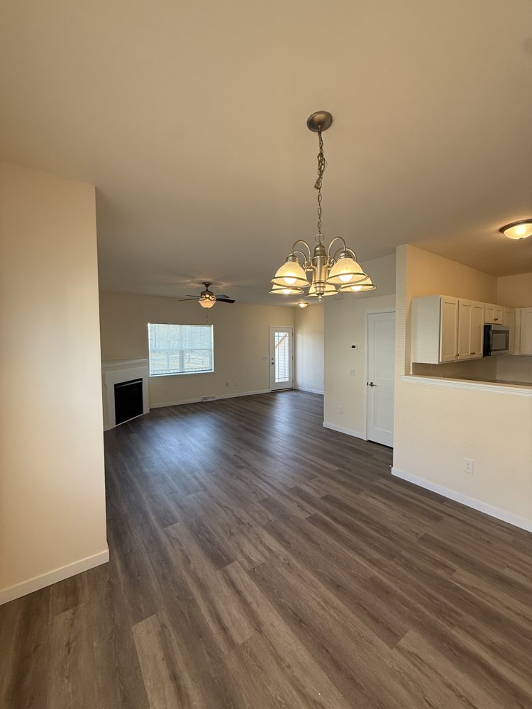 Open living and dining area with dark wood-look plank flooring, a fireplace and a view into the kitchen